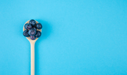 top view of fresh ripe blueberries on wooden spoon on blue background with copy space