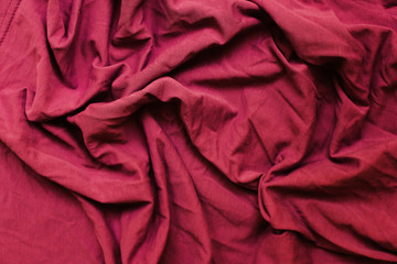Crumpled dark red wavy fabric texture. Dark burgundy red cloth background. Wrinkled clothing...