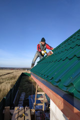 A rooftop worker attaches a metal tile to the roof base.