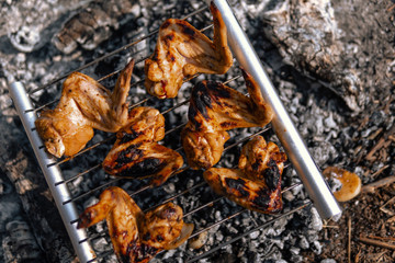 Top view. Lightweight, folding, portable grill for tourism, hiking, takes up little space, durable aluminum and steel. Cooking on a camping trip. Coal and smoke. BBQ Chicken Wings