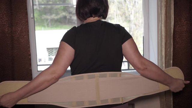 Woman takes off her lumbar corset or posture corrector for women. A wide belt to support the back muscles.