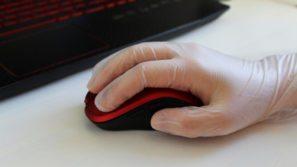 Woman is holding red stylish mouse by her hand, close up. Doctor or nurse or office worker using protective gloves while using computer mouse working at PC at hospital or work in order to stop