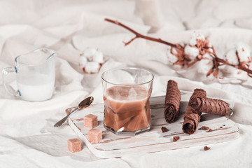 A cup of cold espresso with cream and waffle tubule with chocolate filling in bed. Sweet breakfast, copy space for your text