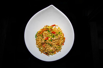 a bowl of spicy wok style chicken and pepper noodles served in a white teardrop bowl