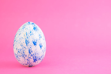 The egg is painted blue on a pink background. Creative card with Easter. Copy space