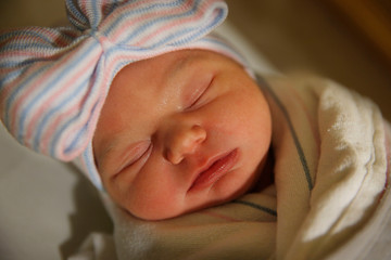 A newborn infant sleeps with a hat on