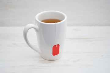 Cup of tea isolated on white wooden  background. Teabag with red label.