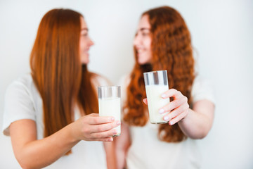 glasses with milk held by two redheaded young women on isolated white backgroung, healthy dieting concept