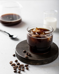 ice coffee with ice cubes in a glass on a light background, coffee beans are scattered nearby