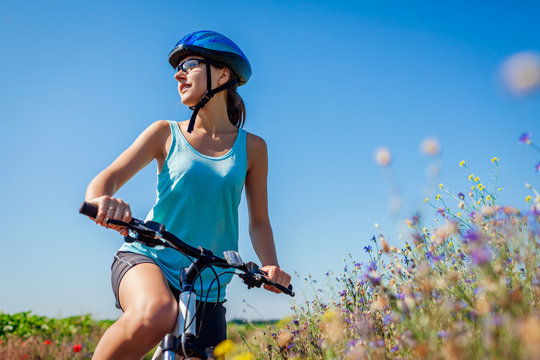 Happy young woman cyclist wearing helmet having rest after riding bicycle in summer field enjoying landscape.
