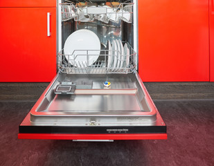 Build-in dishwasher with opened door in a red kitchen.
