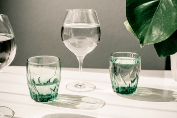 Glasses of water on white table. Harsh light through glasses, shadows. Clean minimalist contemporary art. Conceptual image. Green and white clean colors. Pure water in glass. Simple visual concept.