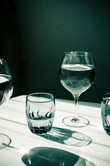 Glasses of water on white table. Harsh light through glasses, shadows. Clean minimalist contemporary art. Conceptual image. Green and white clean colors. Pure water in glass. Simple visual concept.