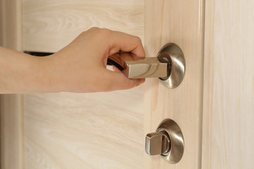 To open the door. Modern white door with chrome metal handle and a female arm. Elements of interior closeup