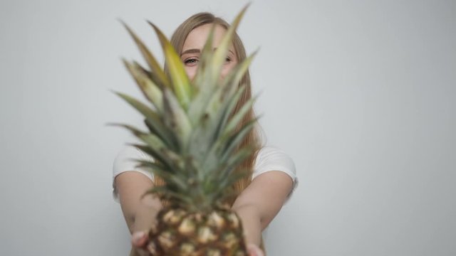 Beautiful girl with pineapple posing in front of camera in bright room