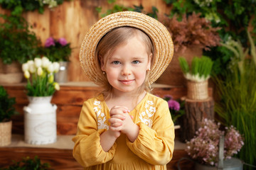 portrait child praying. Little girl hand praying, hands folded in prayer concept for faith, spirituality and religion. Cute little blond girl in a yellow dress and straw hat in garden, summertime. 