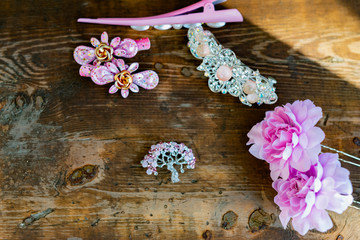 Obraz na płótnie Canvas A composition of women's jewelry and accessories in pink on an old wooden surface. Brooch with colored stones, hairpins and flowers in delicate shades