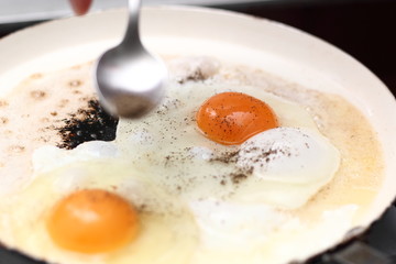 Sprinkle with pepper. Making sunny side up eggs with black pepper and salt.
