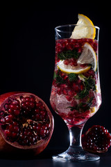 Glass with a cocktail with lemon, mint, and pomegranate seeds, sliced pomegranate on the table.