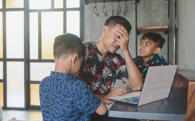 Father working on laptop online from home with kids. Quarantine and closed school during coronavirus outbreak. Noisy children disturb man at work. Homeschooling and freelance job. Home office.