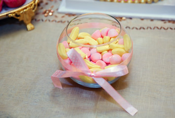 Pink and yellow candies in glass vase on white background . Multicolored round candy sweets in a round spherical vase aquarium Creative concept .