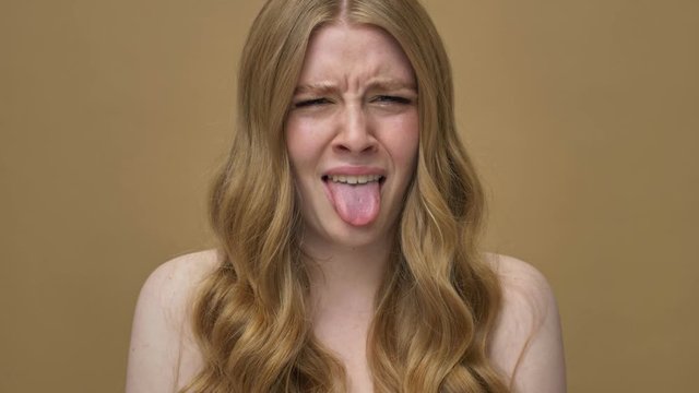 A displeased young half-naked woman with long hair is looking at something disgusting isolated over beige background