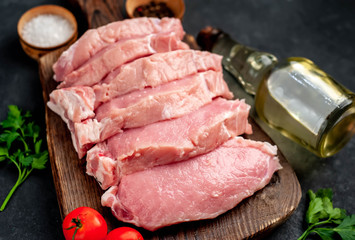raw pork steaks with spices on a cutting board on a stone background