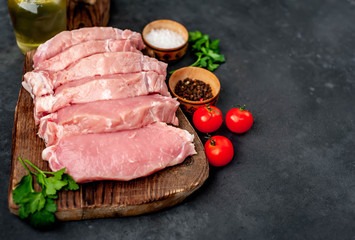 raw pork steaks with spices on a cutting board on a stone background