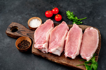 raw pork steaks with spices on a cutting board on a stone background
