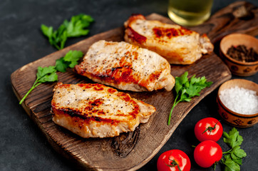 grilled pork steaks with spices on a cutting board on a stone background