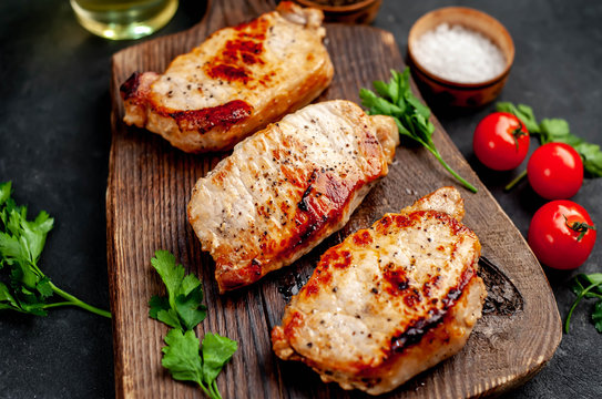 grilled pork steaks with spices on a cutting board on a stone background