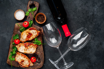 Dinner for two, grilled pork steaks with spices, a bottle of wine and glasses on a stone background