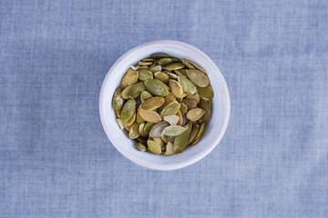 Pumpkin seeds a source of healthy fats, plate on a gray background. Healthy snack instead of sugar for tea or coffee drink. Top view