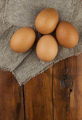 Eggs stand on a burlap that stands on a brown wooden table. Top views with clear space