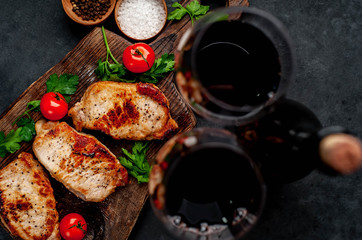 Dinner for two, grilled pork steaks with spices, a bottle of wine and glasses on a stone background