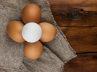 Eggs stand on a burlap that stands on a brown wooden table. Top views with clear space