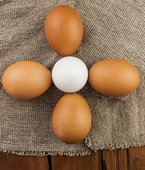 Eggs stand on a burlap that stands on a brown wooden table. Top views with clear space