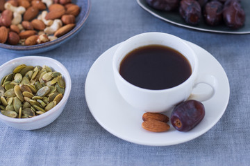 White cup americano coffee with healthy snacks in small plates on gray background. Best alternative to bad sweets and no sugar. Cashew nuts, almonds, dates, seeds. Raw vegan dessert for diet.