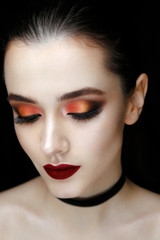 Close-up portrait of gorgeous young woman with red lips and bright makeup of eyes. Beautiful girl with a healthy clean skin against black background.