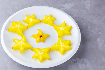 Carambola on a white plate. Sliced carambola on a gray background. Slices of star fruit. Trendy...