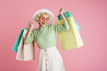 Spring shopping concept: happy smiling fashionable woman wearing trendy clothes posing with colorful paper bags. Pink background. Copy, empty space for text - 338893884