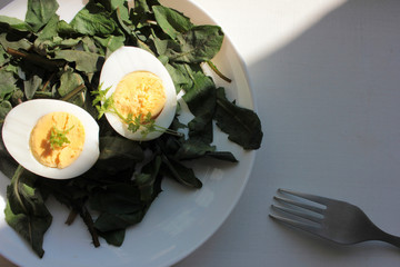 Spring salad with fresh dandelion greens and hard-boiled eggs in white plate on white wooden...