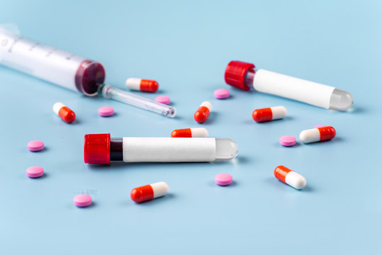 Two vacuum blood test tubes with a blank label for inserting text, a syringe and tablets on a blue background. The concept of a coronavirus or covid-19