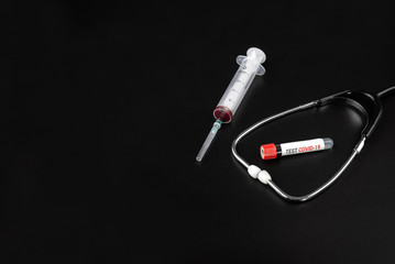 Blood sample tube with the text Test COVID-19, stethoscope and syringe on a black background. The concept of coronavirus or 2019-nCov.