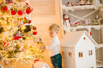 Cute little boy with blond hair plays toys in a bright room decorated with Christmas garlands near the Christmas tree. Happy childhood. Christmas mood
