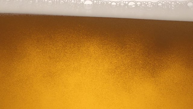 Close-up of the contents of a glass of beer. Beer slowly sways in a glass, waves, bubbles and foam.