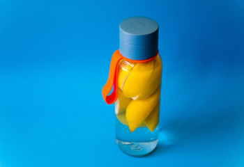 Flat lay style concept of healthy lifestyle, sport and fitness at home. Bottle of water with lemons on blue background