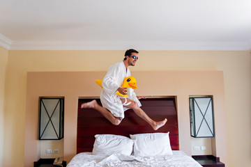 The guy in the bathrobe, the swimming glasses with the duck on the belt and the cup of coffee jumps on the big bed in the hotel room. Remote work at home. Self-insulation. I dream of a vacation.