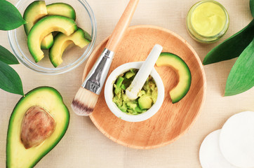 Making skincare treatment product with fresh ripe green avocado, mixed in mortar crushing food slices, wooden bowl cosmetic brush facial mask healthy beauty treatment, top view overhead background. 