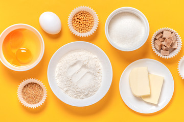 Fototapeta na wymiar Ingredients for baking on a orange background, top view, copy space. Flour, eggs, sugar and butter in white bowls. Cooking and baking concept, flat lay.